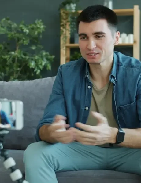 A man on his couch at home, talking to his phone camera