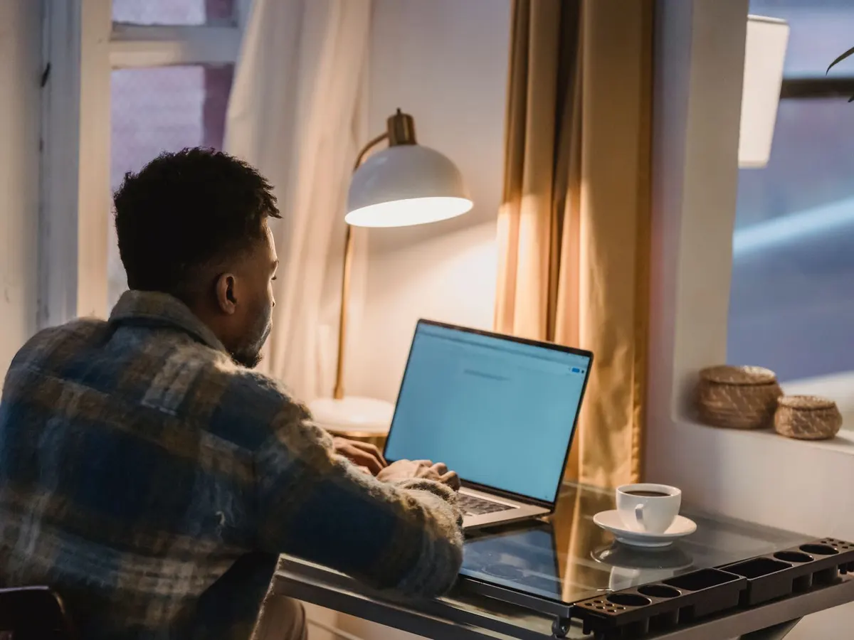 A man working on his laptop at night, with a lamp and a coffee